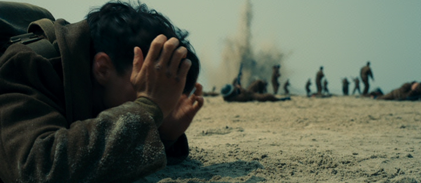 Fionn White as Tommy Covering His Head as Bombs Land on the Beach